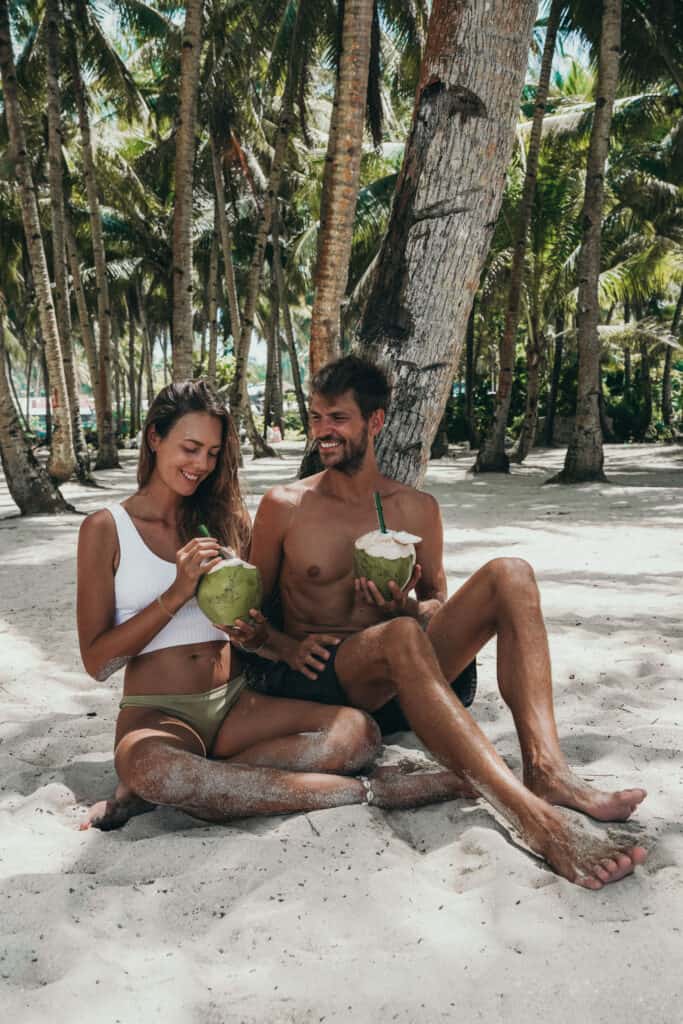 Couple drinking coconuts under palm tree on Daku Island Siargao