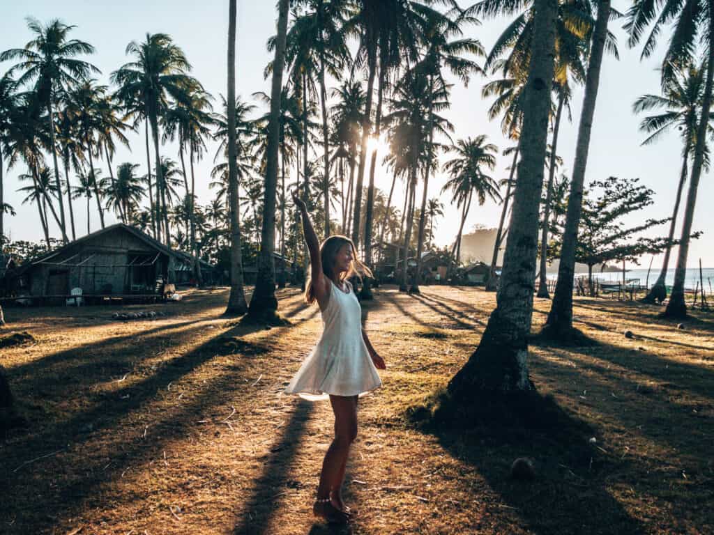Women is dancing between palm trees at Nacpan Beach El Nido Philippines