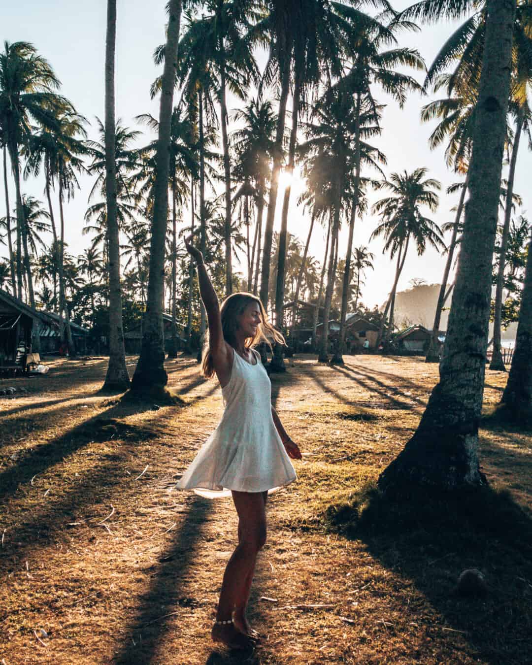 Women is dancing between palm trees at Nacpan Beach El Nido Philippines