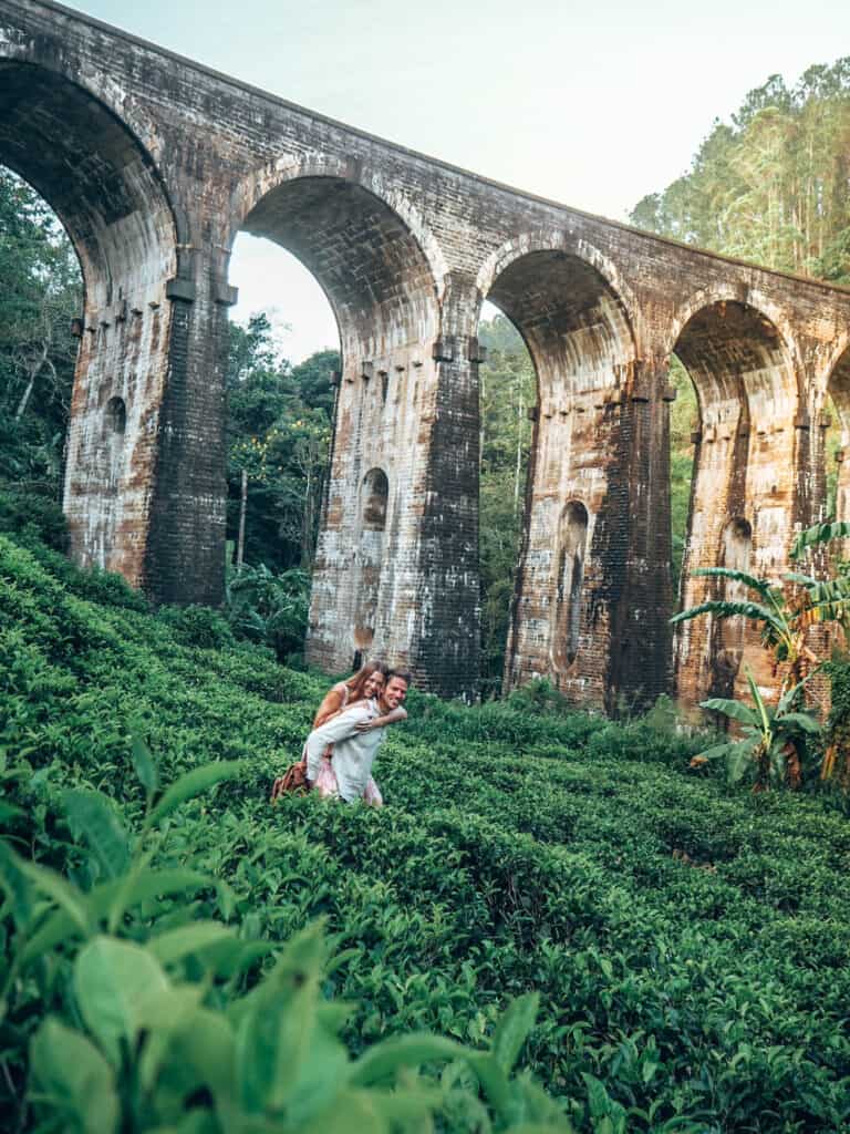 Couple in tea field in front of nine arches bridge ella