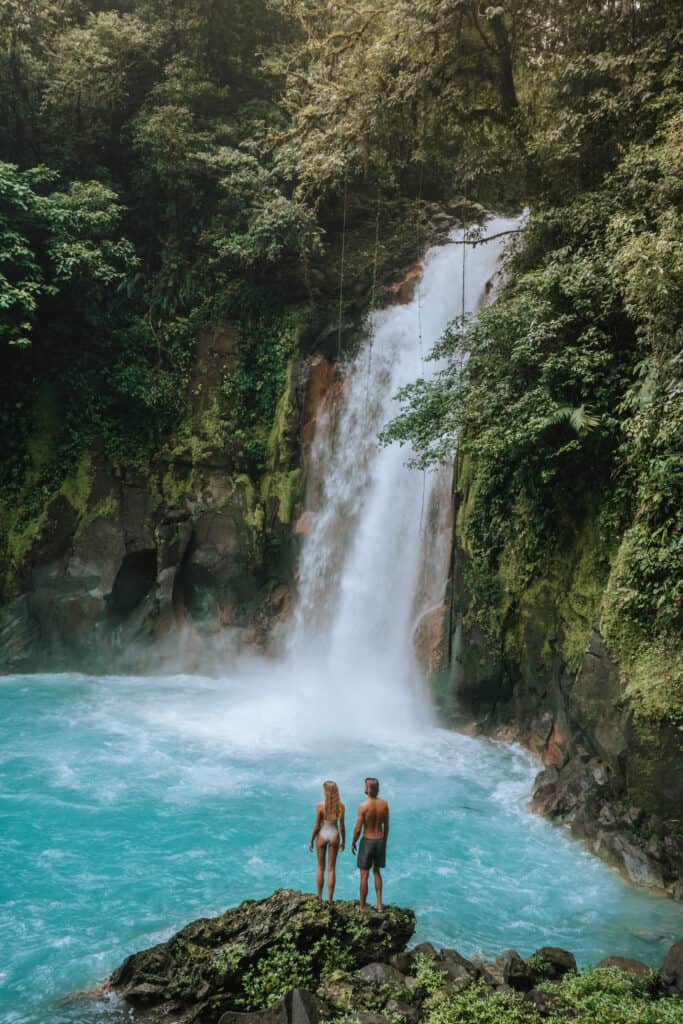 Two people standing in front of a waterfall.