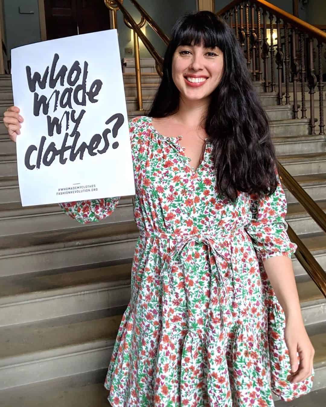 A woman promoting sustainable clothing by holding up a sign questioning its origin.