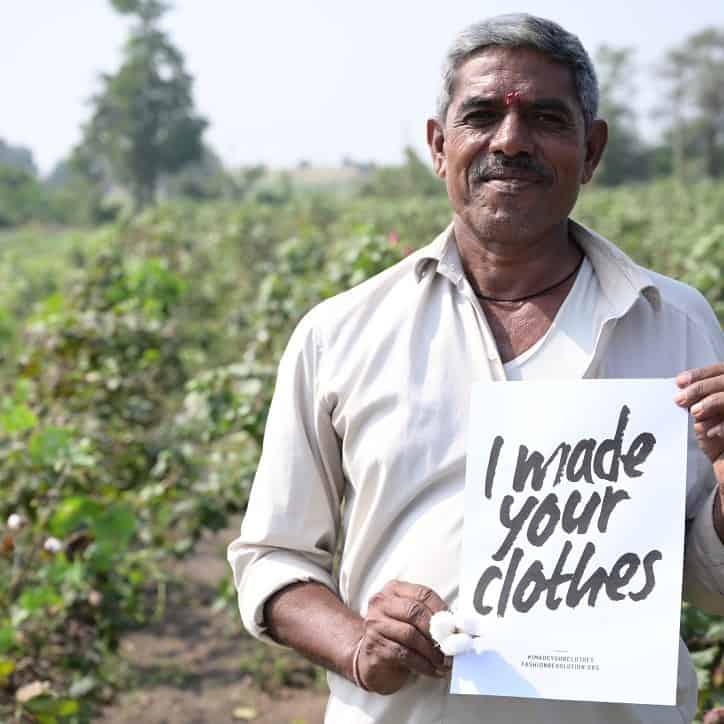 A man promoting sustainable clothing by proudly holding up a sign stating "I made your clothes.