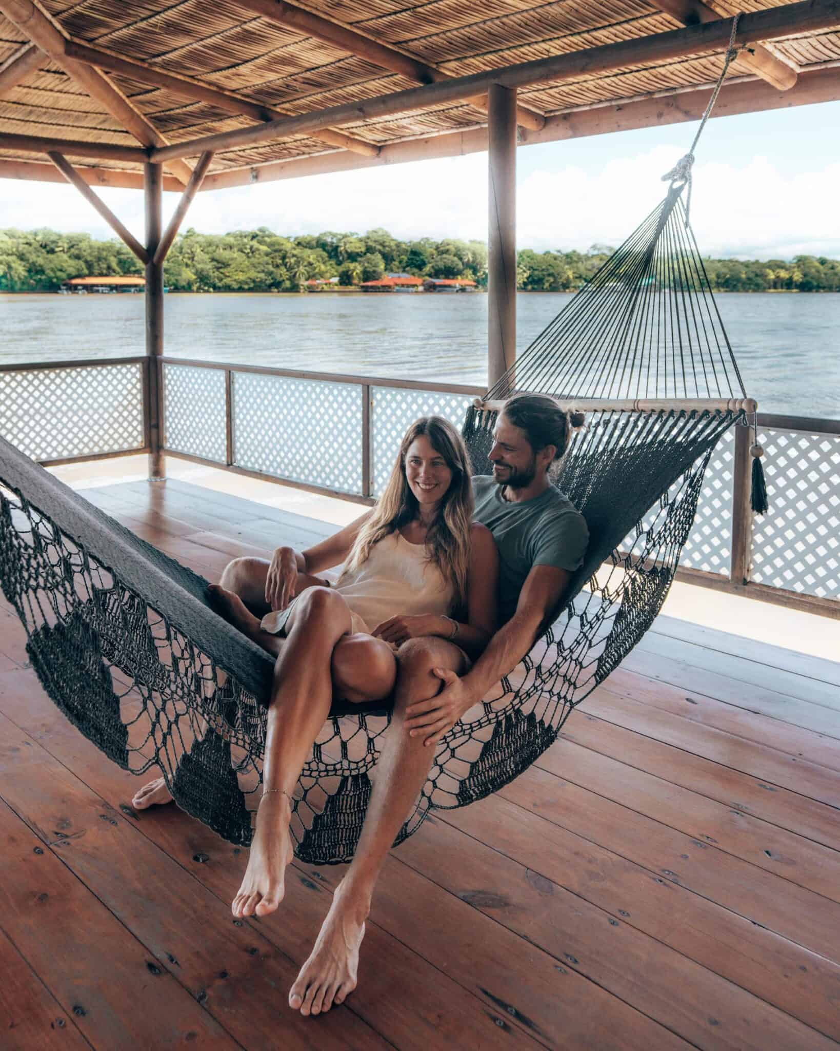 A couple relaxing in a hammock on a wooden deck in Tortuguero, Costa Rica.
