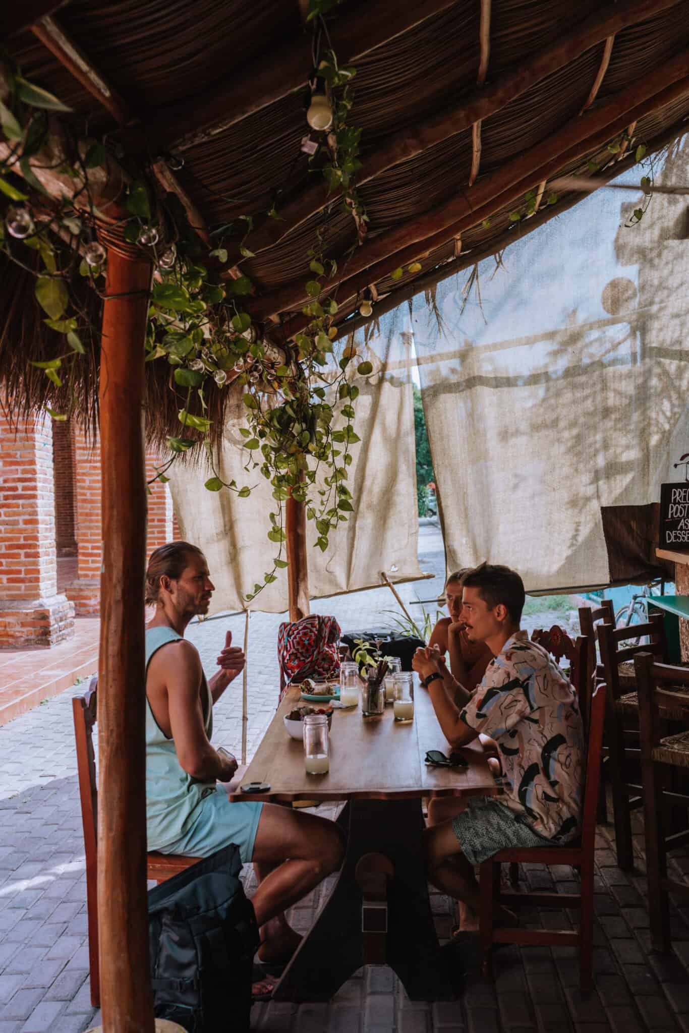 Three people sitting at a table under a thatched roof in Sayulita.