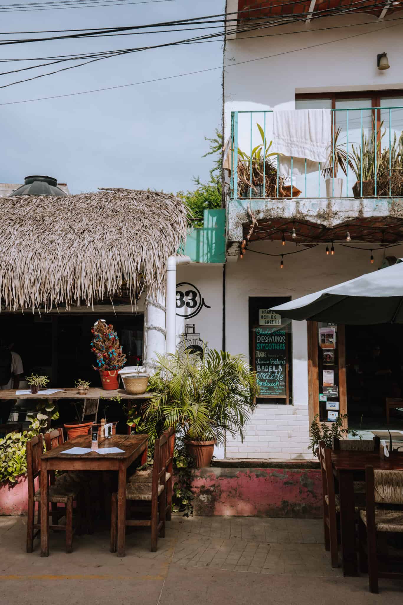 A Sayulita restaurant with tables and chairs in front of a thatched roof.