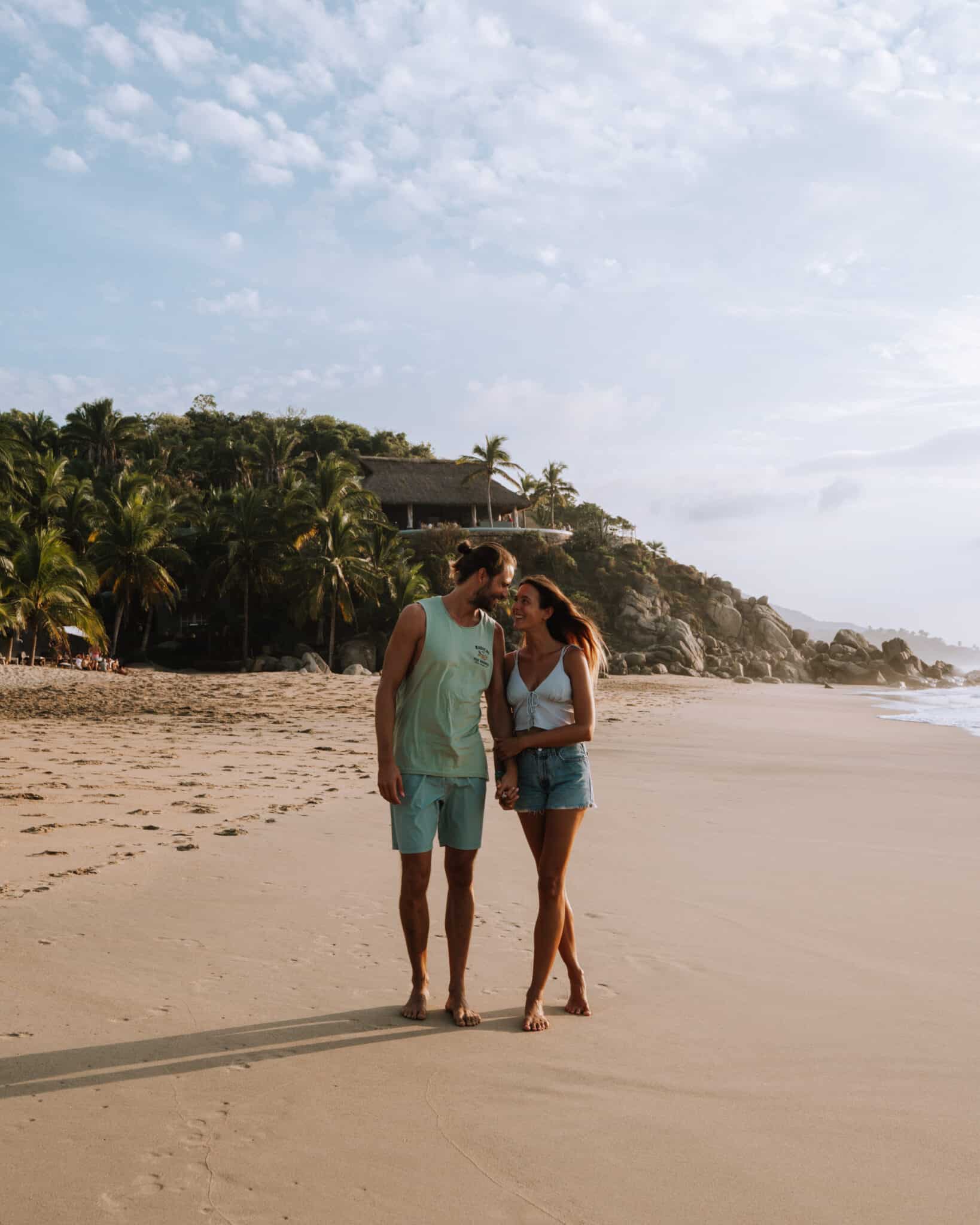 A couple standing on a Sayulita beach with palm trees in the background.