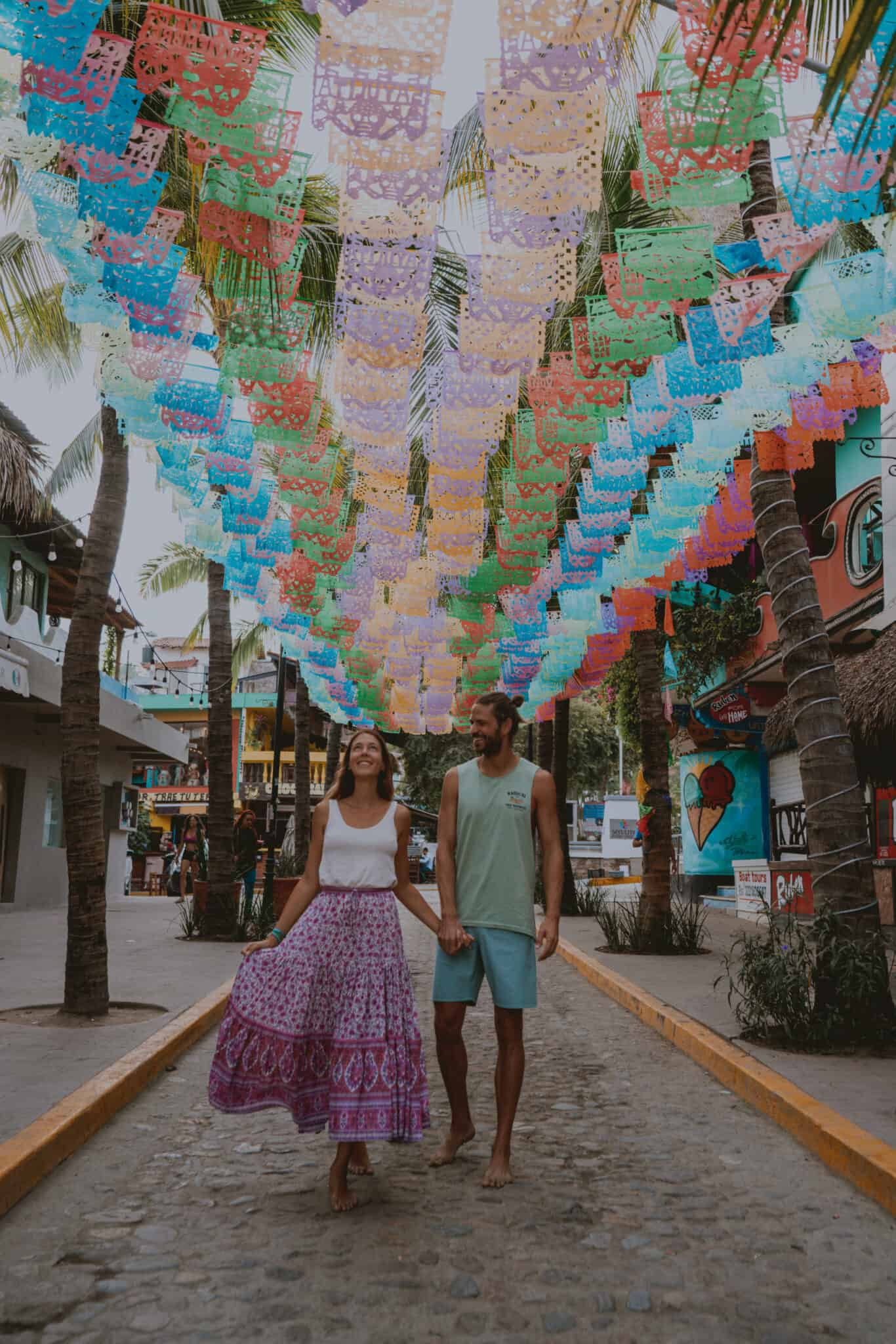 A couple strolling through the vibrant Sayulita streets with papel picado adorning above.