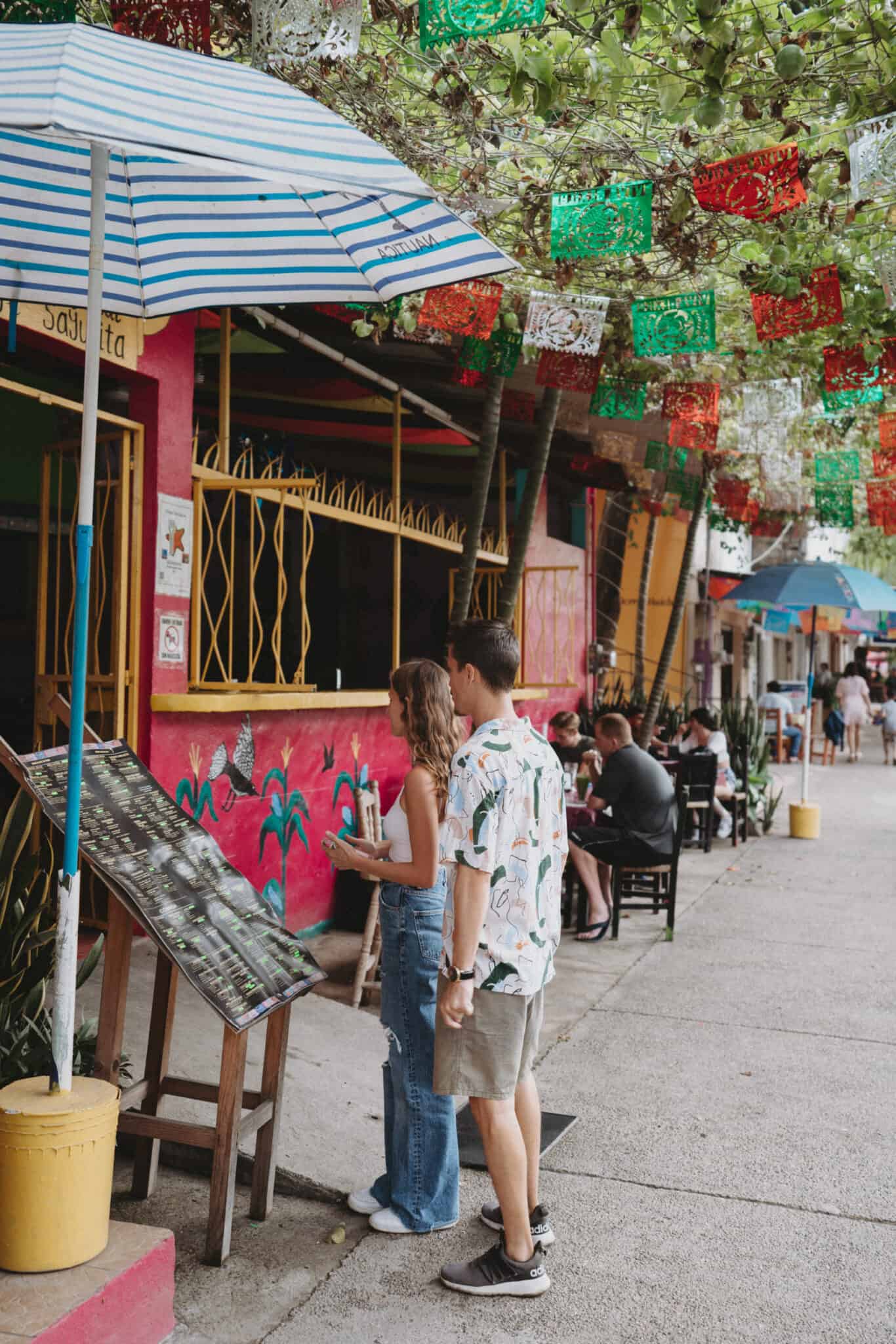 A group of people standing on a sidewalk near a restaurant in Sayulita.