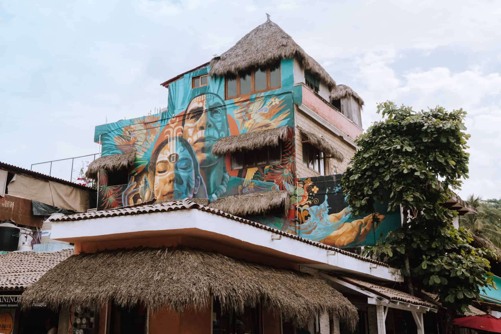 A Sayulita building with a mural on it and a thatched roof.
