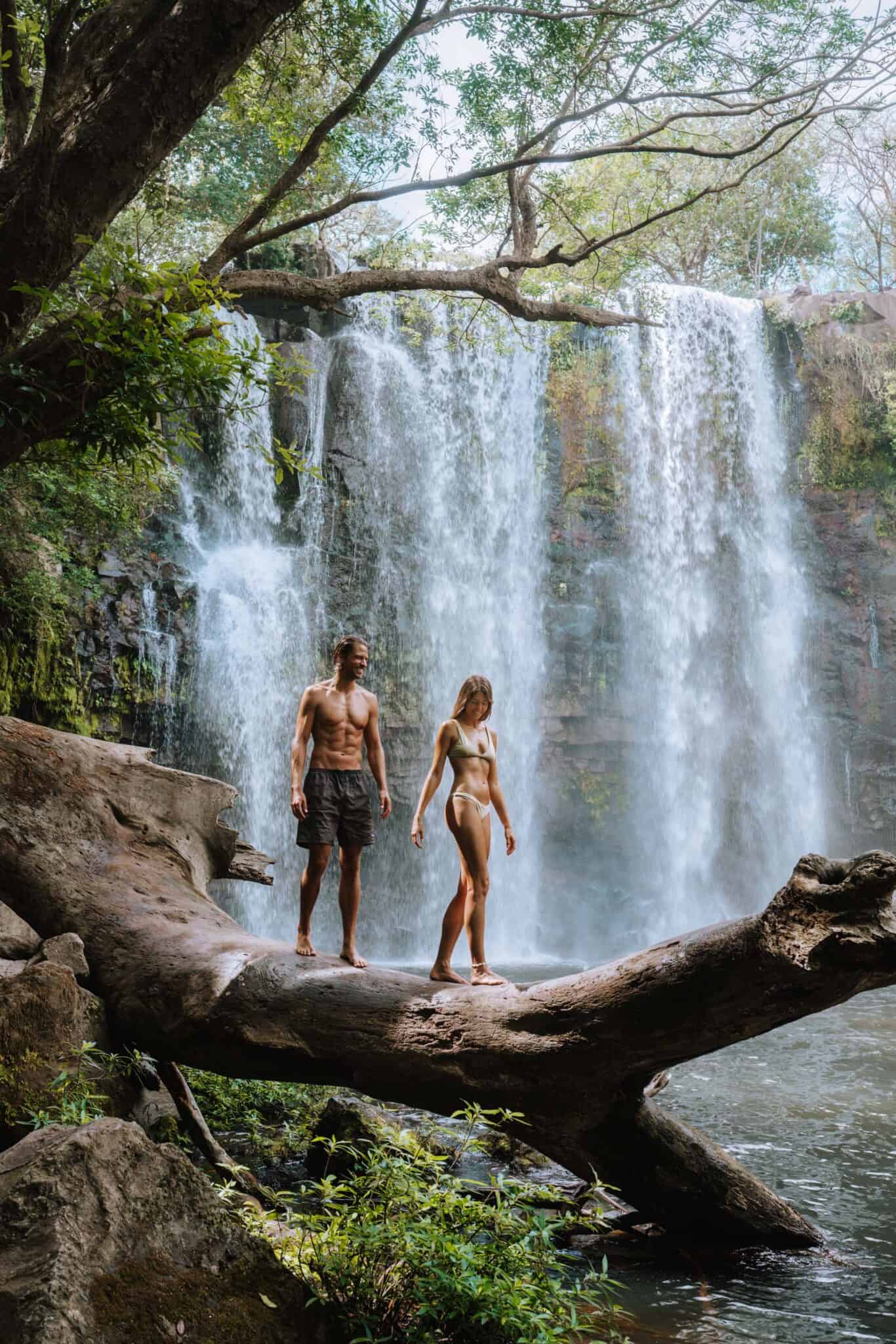 Two people balancing on a log near a Costa Rican waterfall.