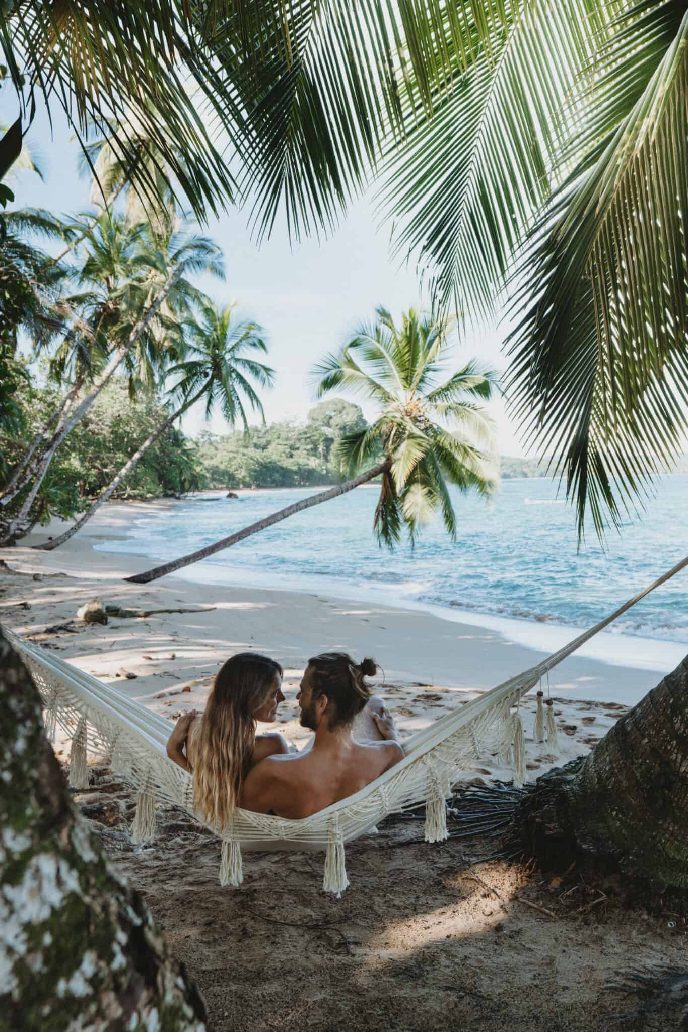 Two people relaxing in a hammock on a beach in Puerto Viejo, Costa Rica.