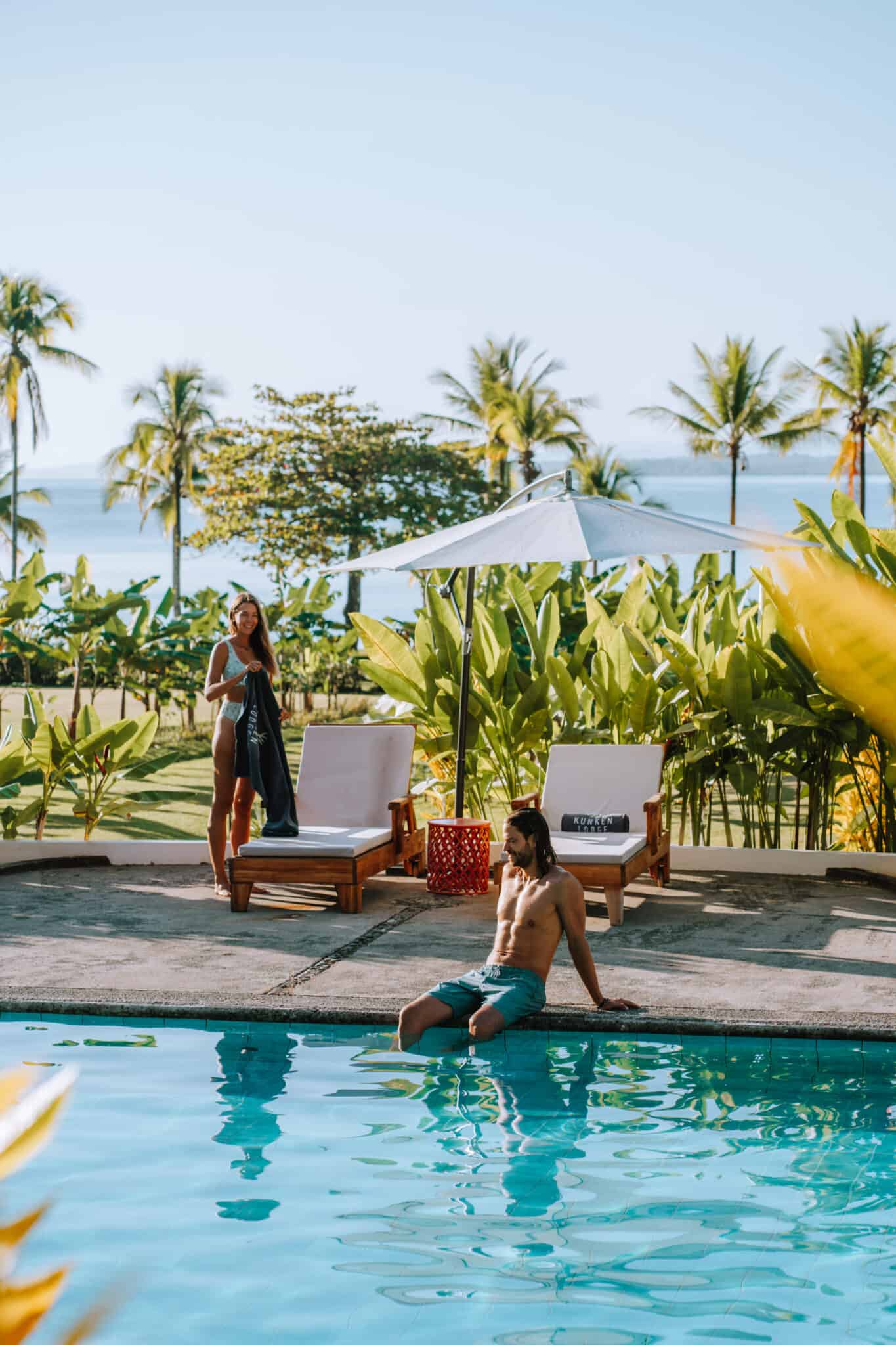 Two people sitting in a pool with palm trees in the background, inviting you to work with us.