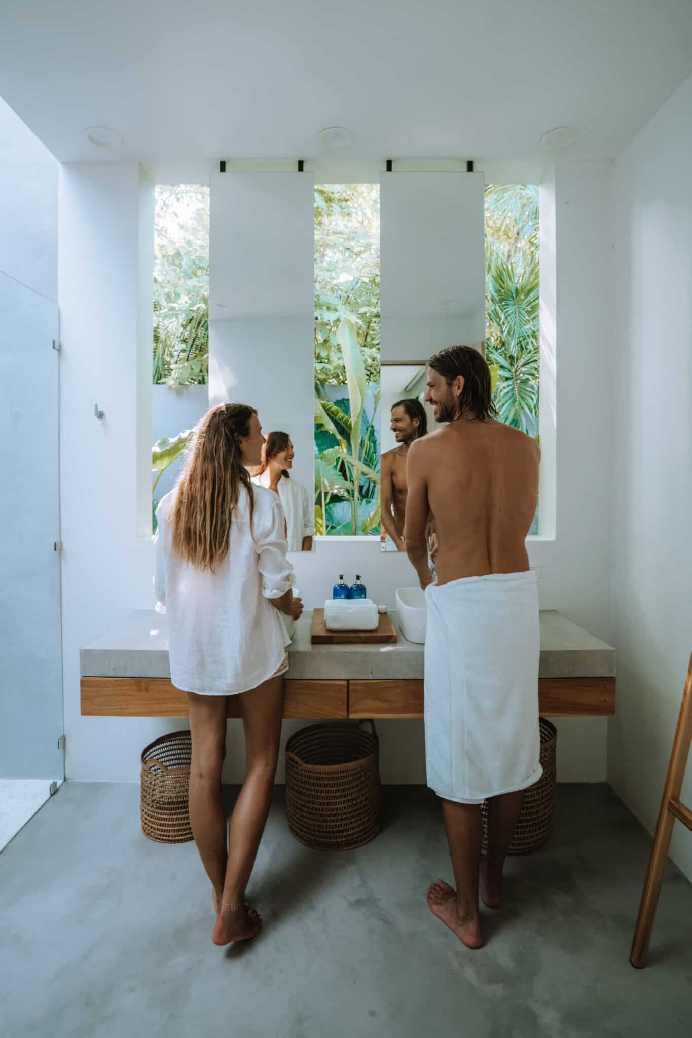 Two people work together in front of a bathroom mirror.