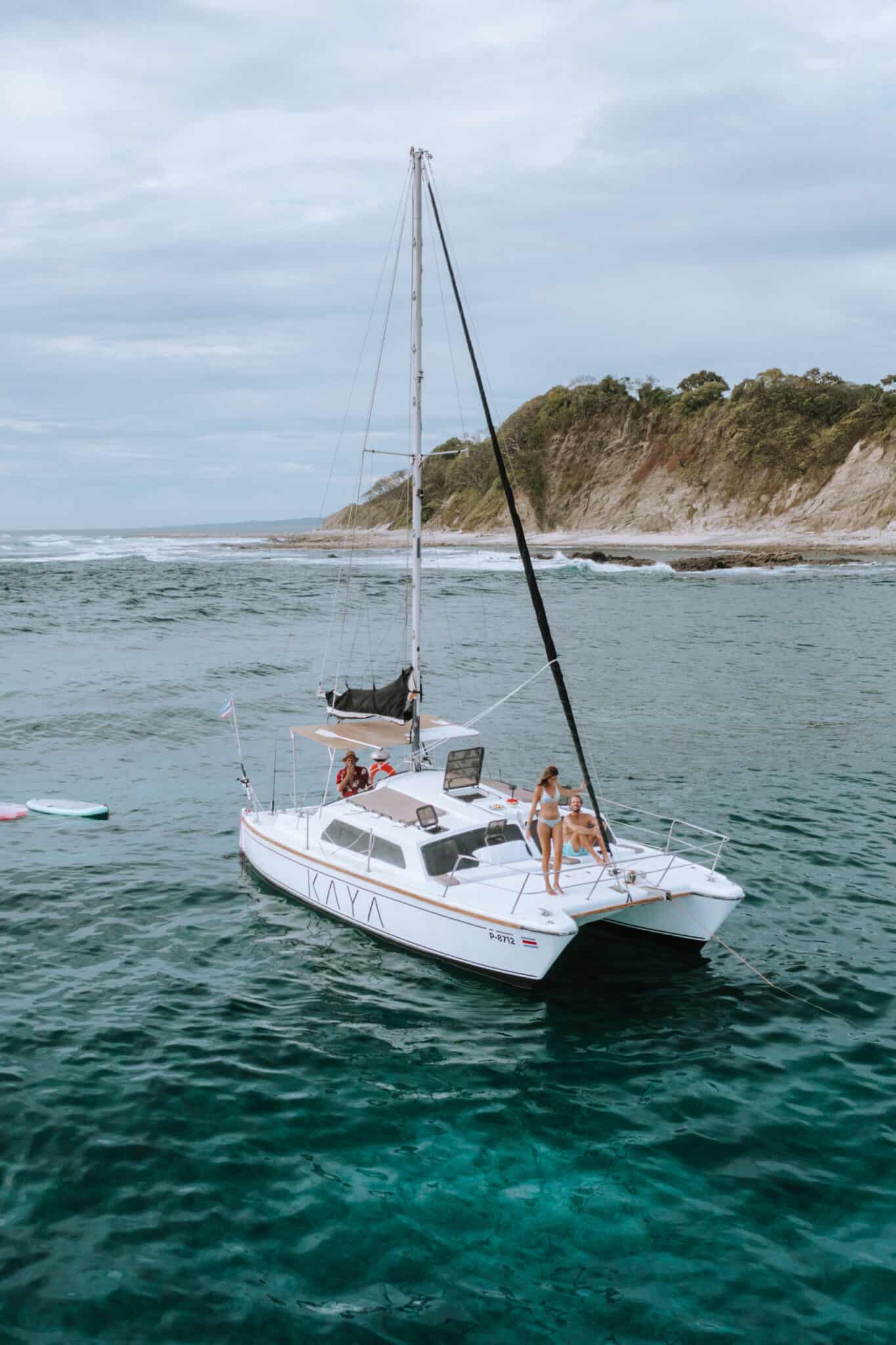 A white catamaran with people on board sails in the ocean, ready to work with us.