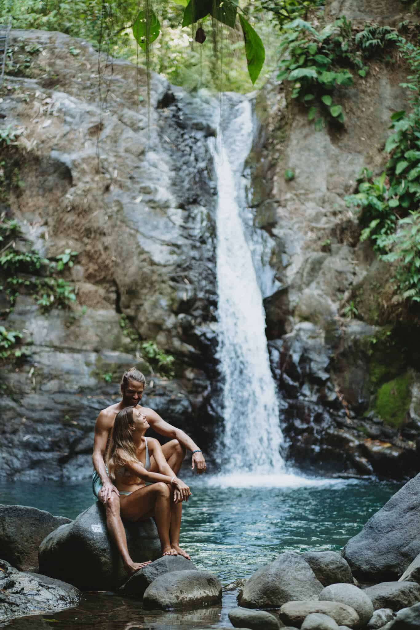 A couple sitting on rocks near a waterfall in Uvita, Costa Rica.