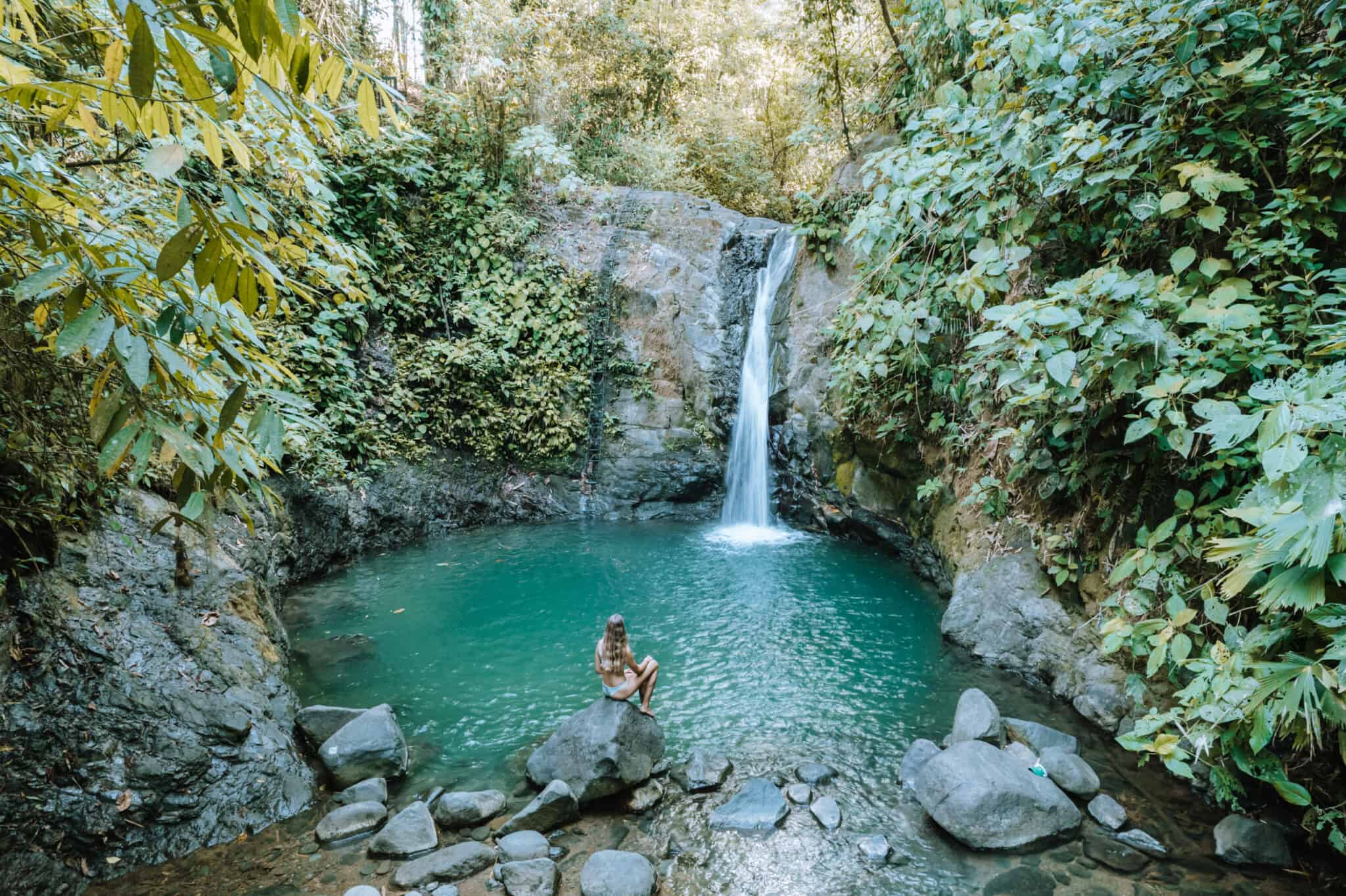 A woman sits on rocks near a waterfall in Uvita, Costa Rica.