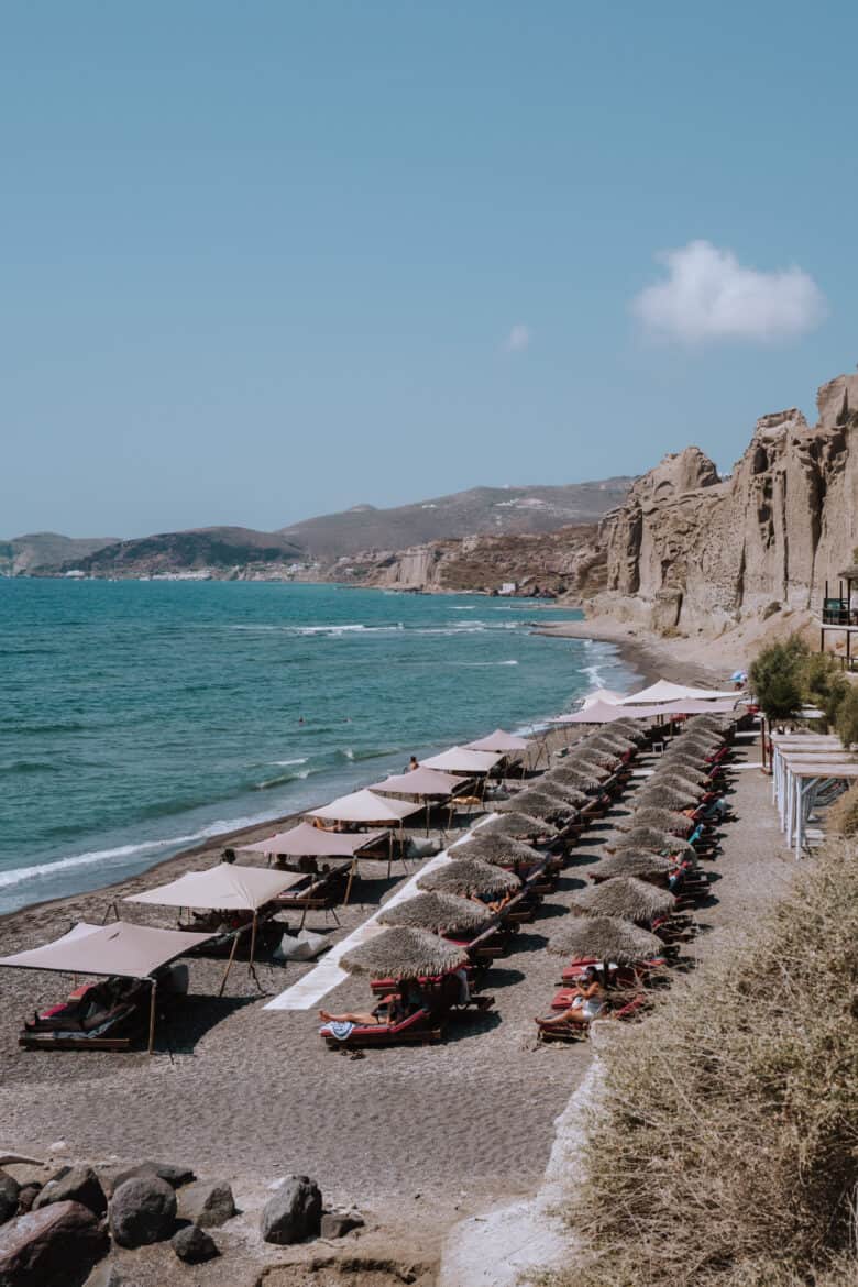 An off the beaten path beach on Santorini with lounge chairs and umbrellas on the sand.