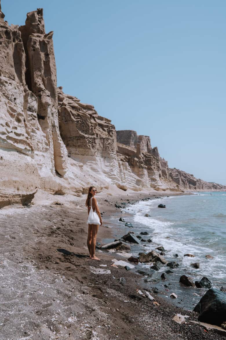 A woman standing on a secluded beach near cliffs in Santorini.