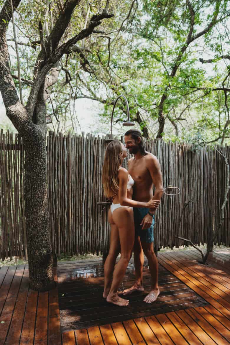 A couple enjoying eco travel at Rhino Sands in South Africa, standing on a wooden deck in front of a tree.