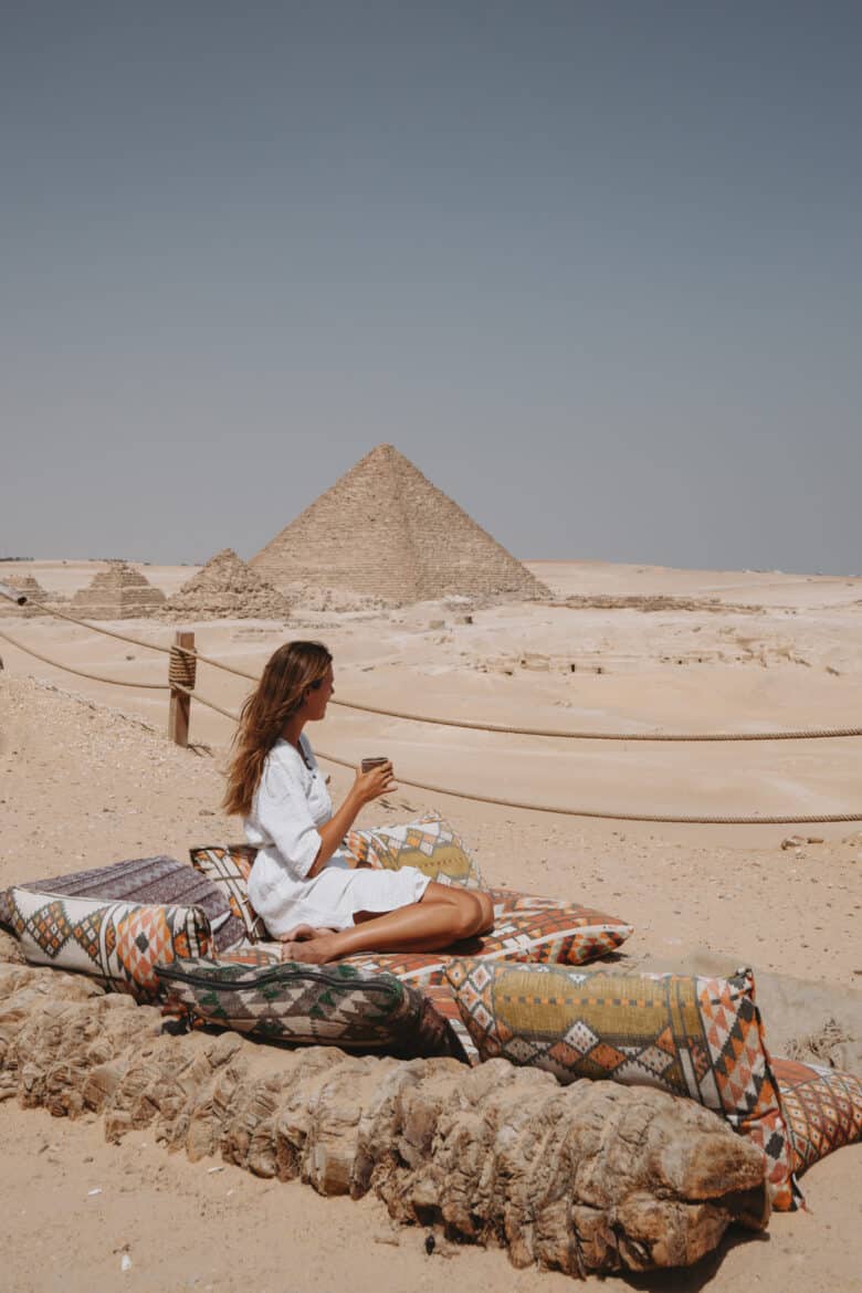 A woman posing on a bed overlooking the Pyramids of Giza.