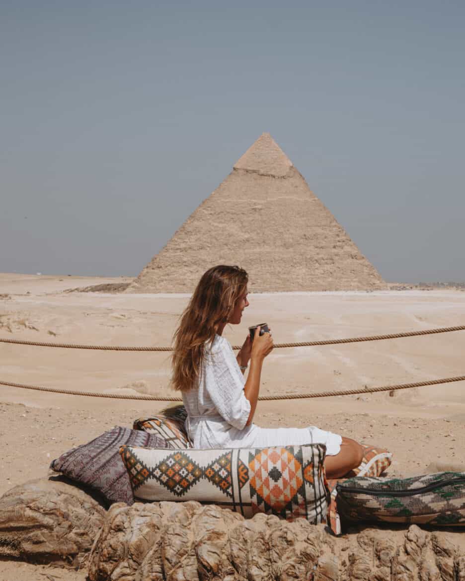 A woman is sitting on a blanket in front of the Pyramids of Giza.