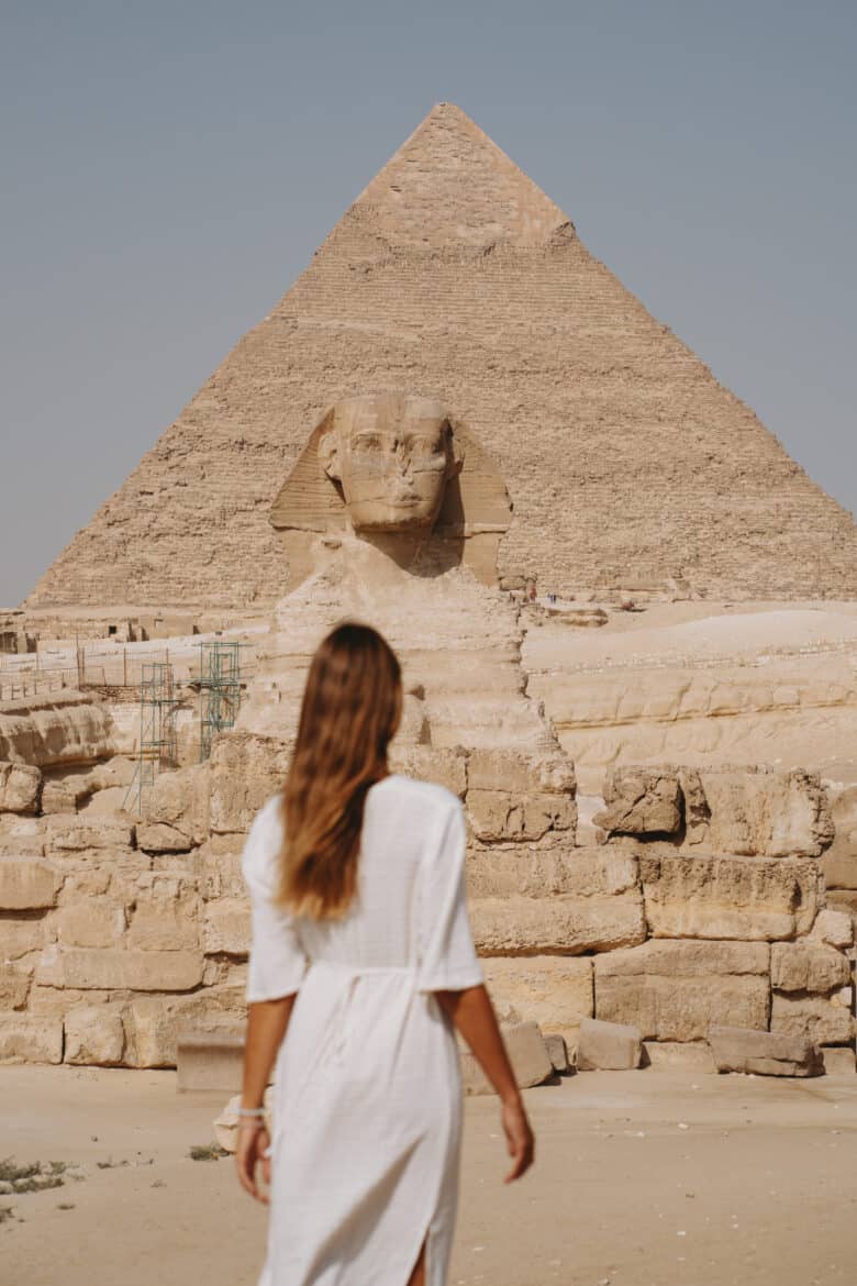 A woman in a white dress strolls in front of the majestic Pyramids of Giza as part of her Egypt itinerary.