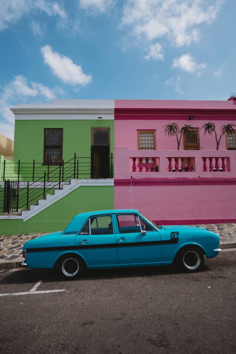 A blue car parked in front of a colorful house.
