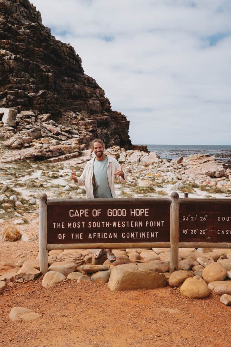 A woman standing in front of the iconic Cape of Good Hope sign in Cape Town, South Africa.