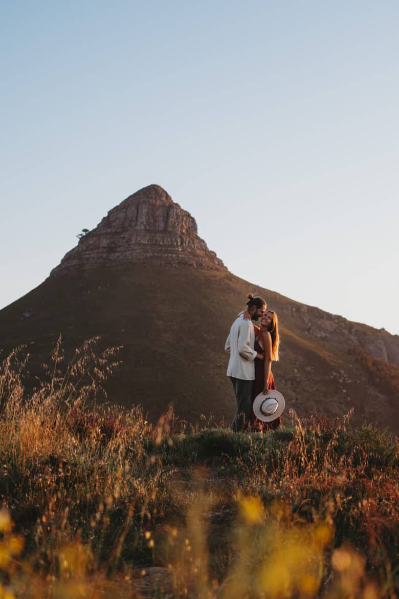 A couple kissing on a hill in front of a mountain.