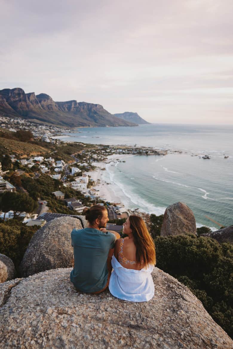 A couple sitting on top of a rock overlooking the ocean.