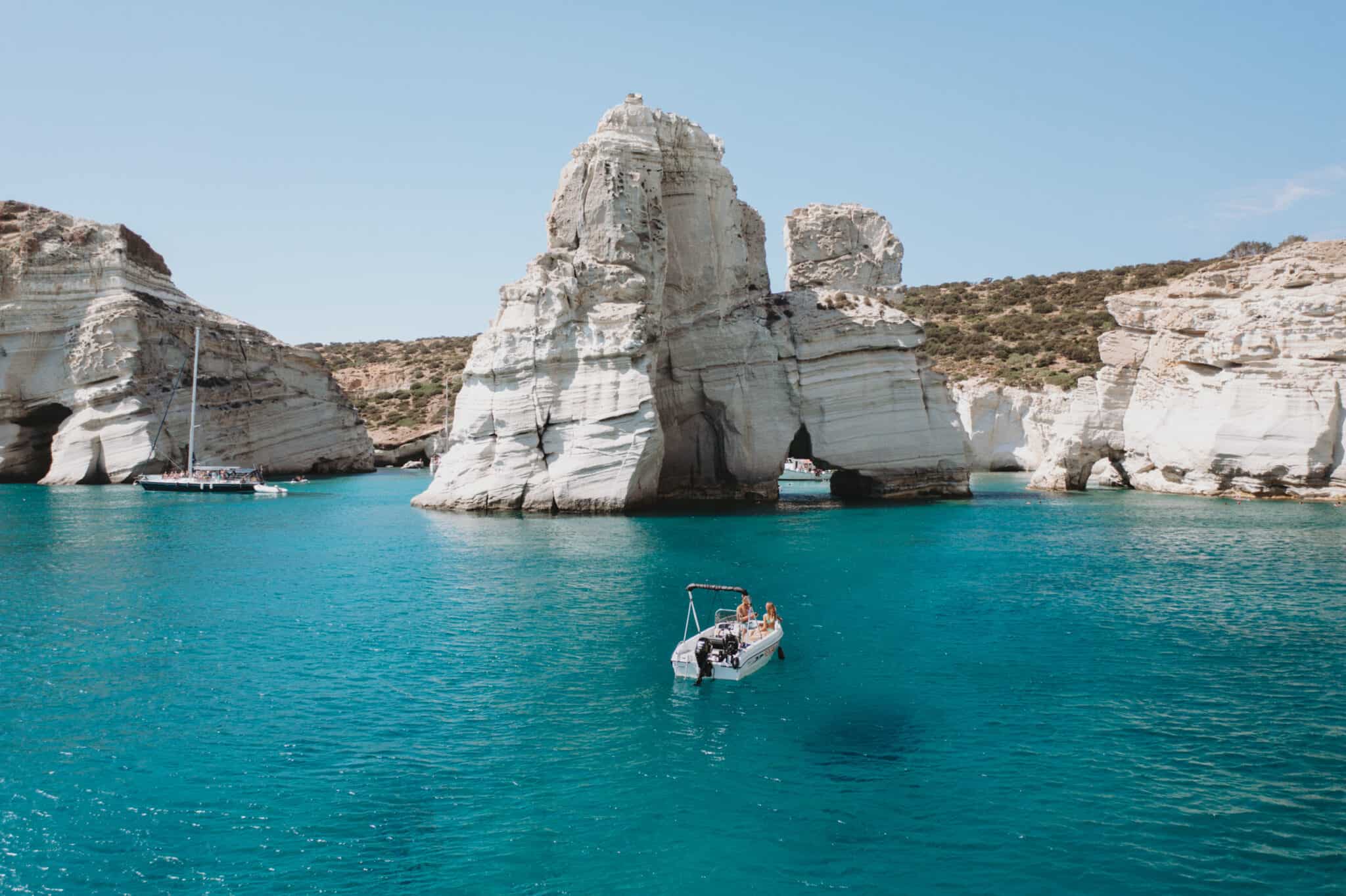 A boat is near a rock formation on Milos island, Greece.