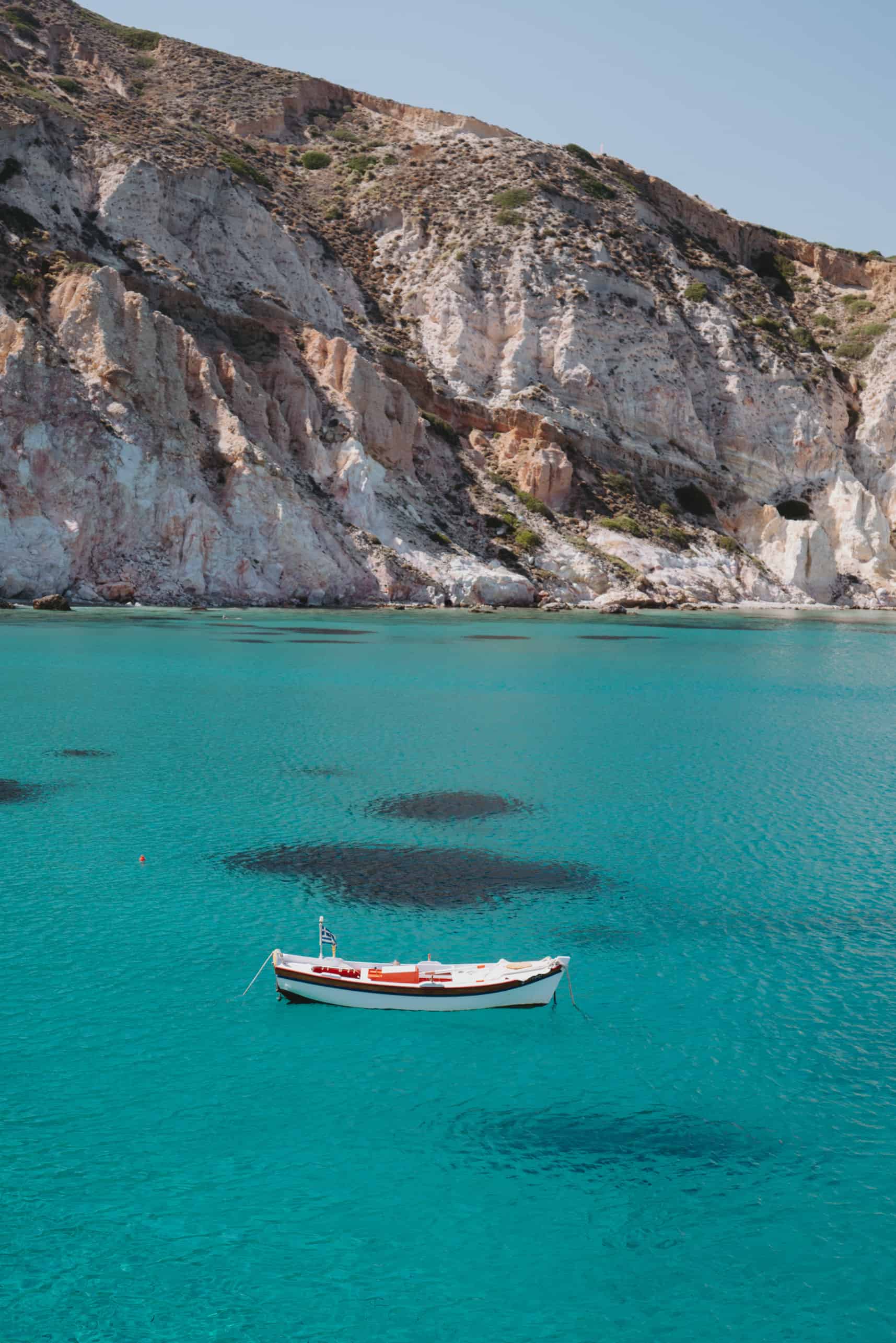 A small boat floats near a cliff on Milos Island, Greece.