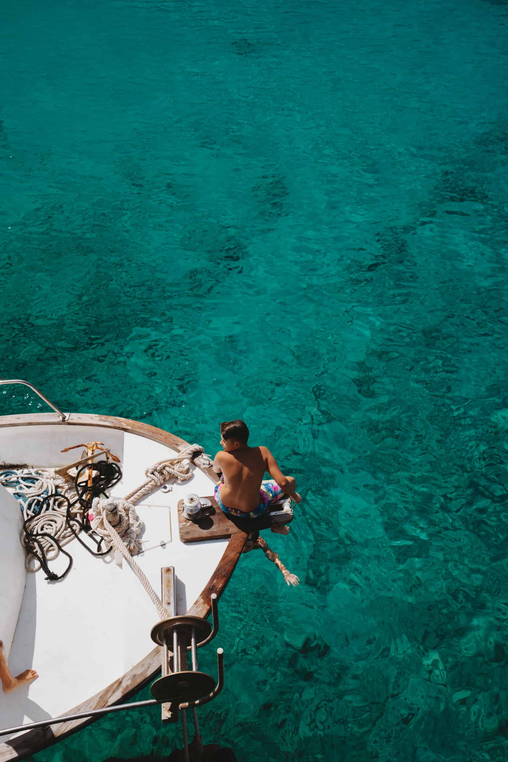 Two people sitting on a boat in the clear blue waters of Milos Island.