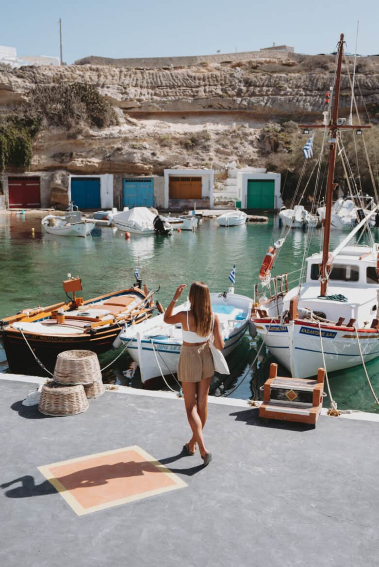 A woman posing in front of boats at Milos Harbor, Greece.