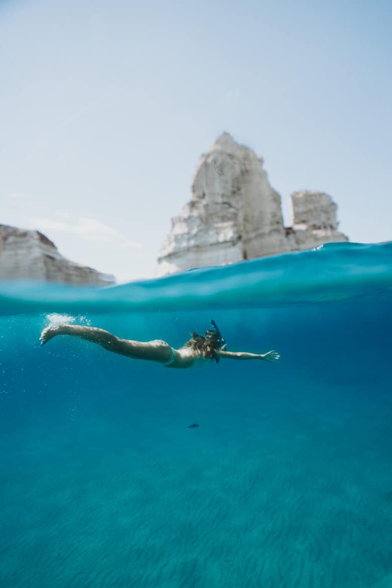 A woman is swimming near a rock at Milos Island, Greece.