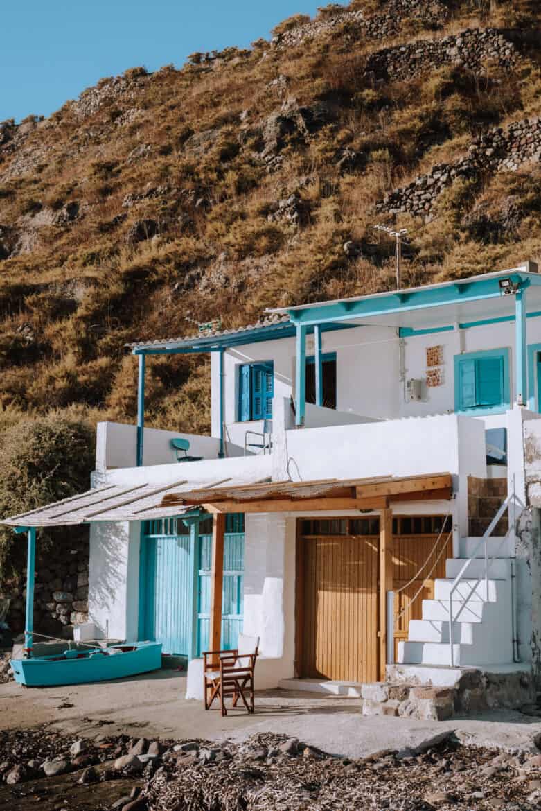 A white house with blue shutters on the hillside of Milos island in Greece.