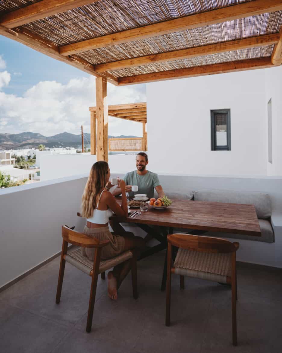 A couple sitting at a table on a balcony overlooking the sea in Milos, Greece.