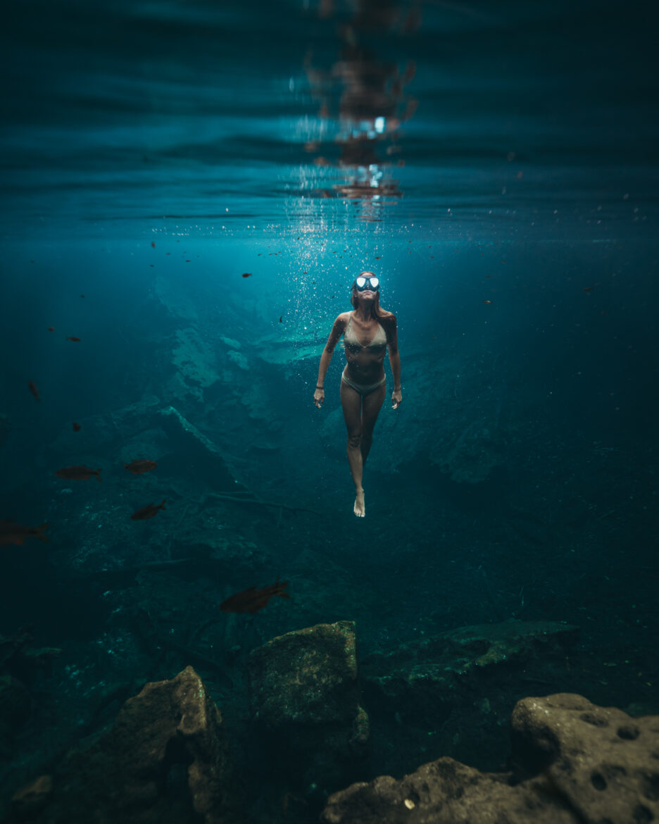 A woman is swimming in the water near rocks.