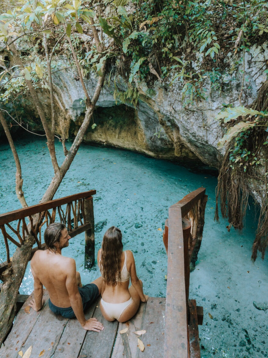 A couple sits on a wooden bridge overlooking a blue lagoon.