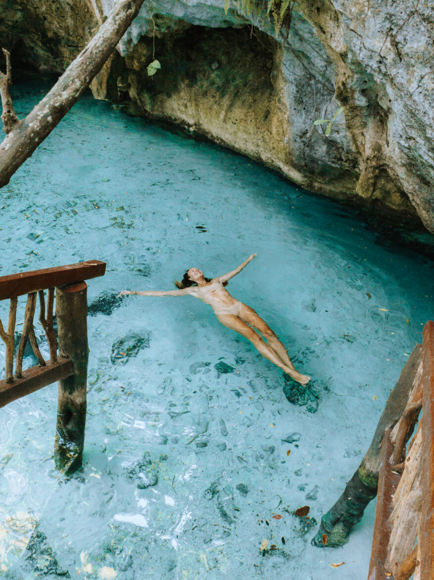 A woman floats in the blue water of a cave.