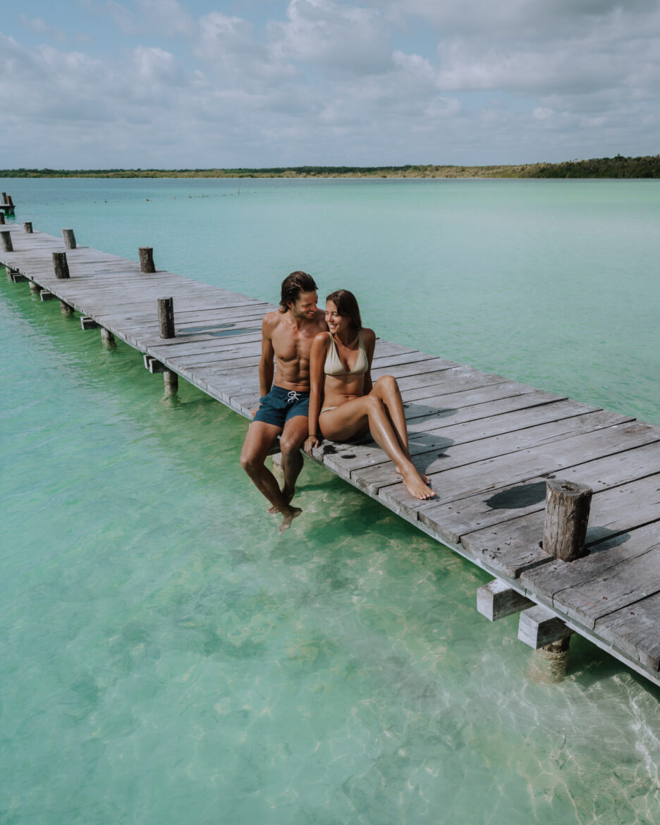 A couple sitting on a dock in the turquoise water.
