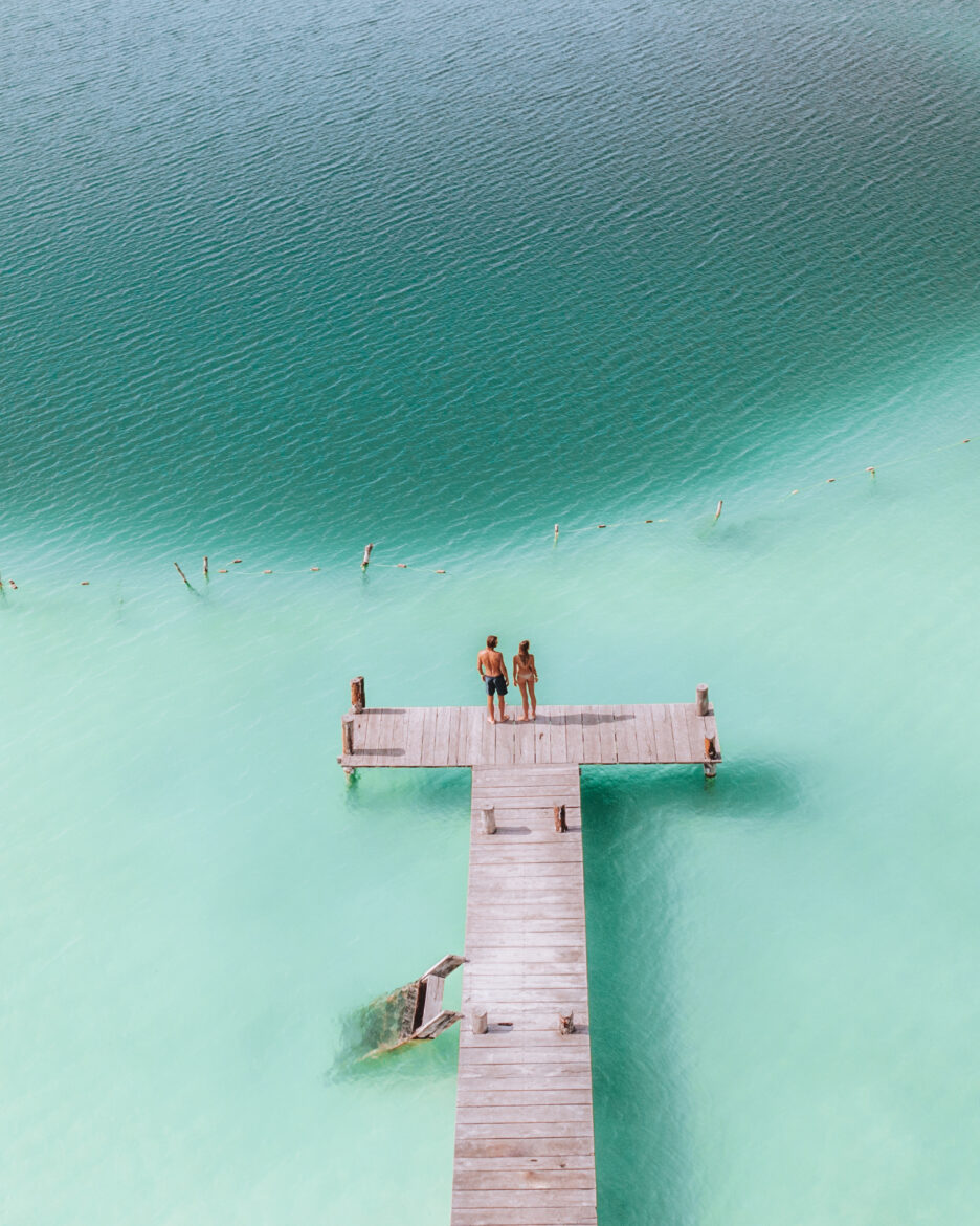 Two people standing on a dock in turquoise water.