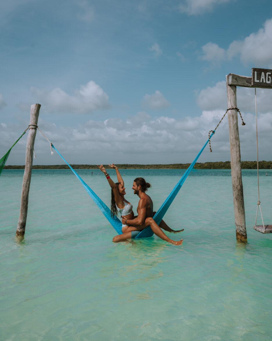 Two people sitting in a hammock in the water.