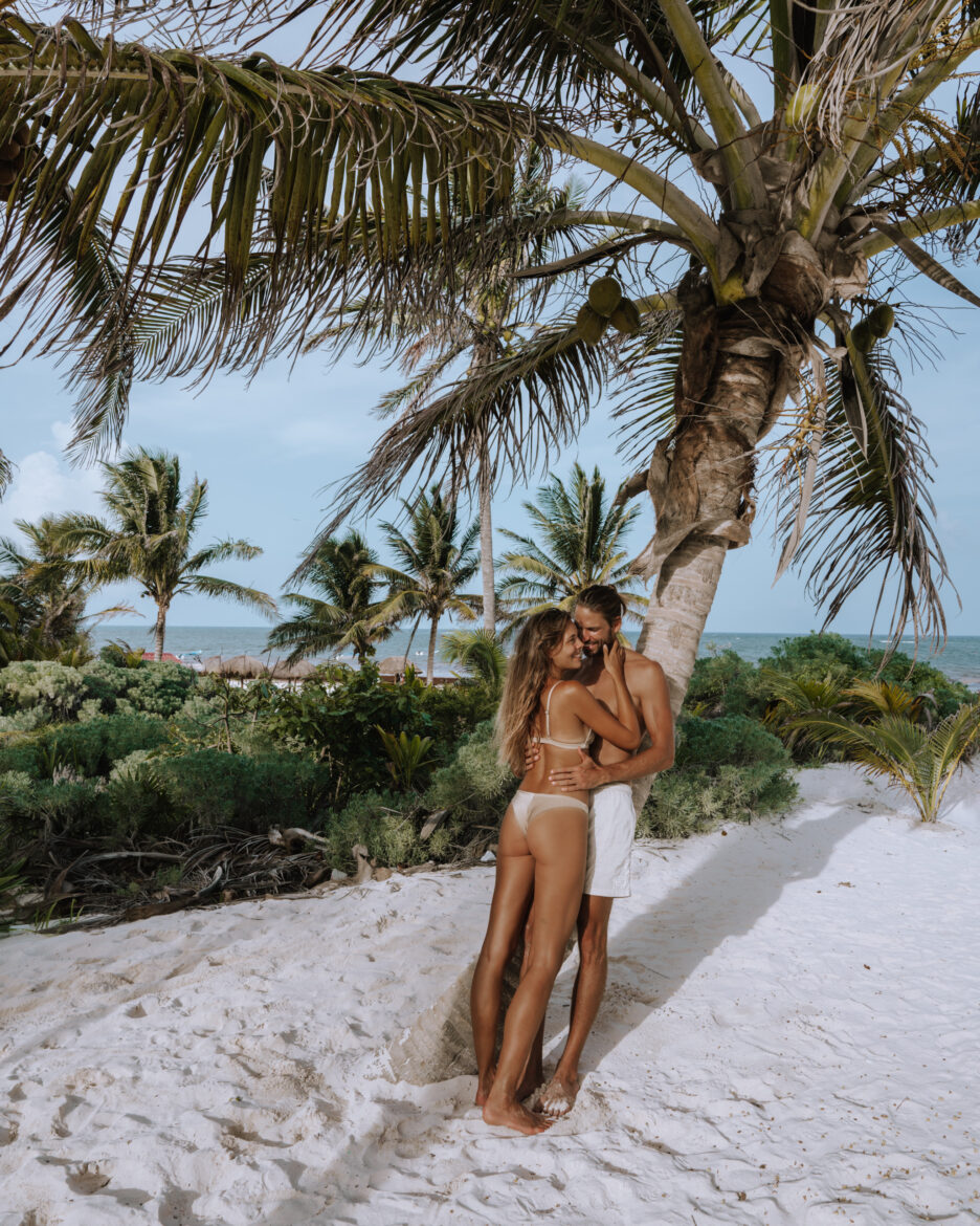 A couple embracing under a palm tree on the beach.