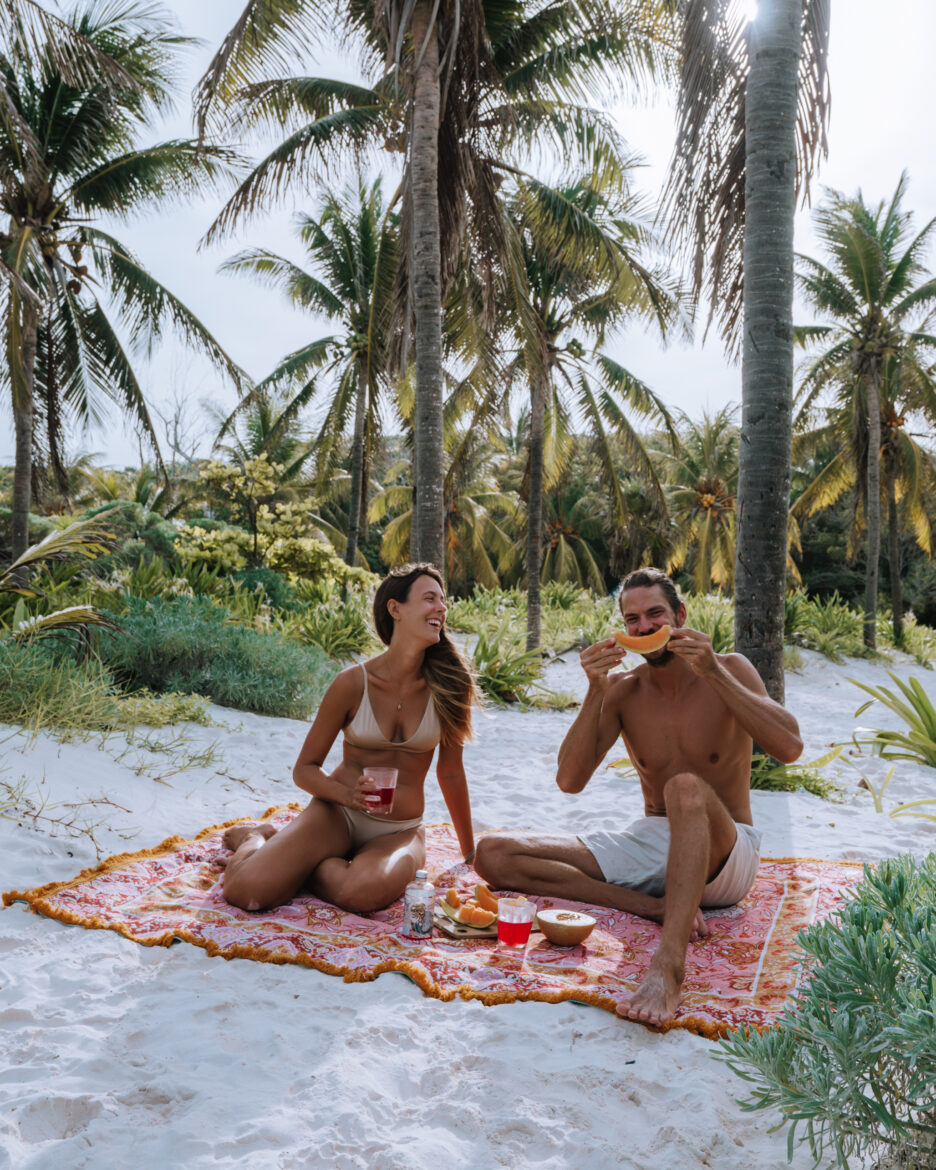 A man and woman sitting on a blanket on the beach.