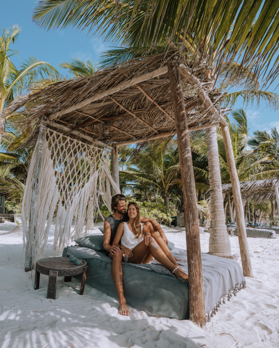 A couple sitting on a bed on the beach in mexico.