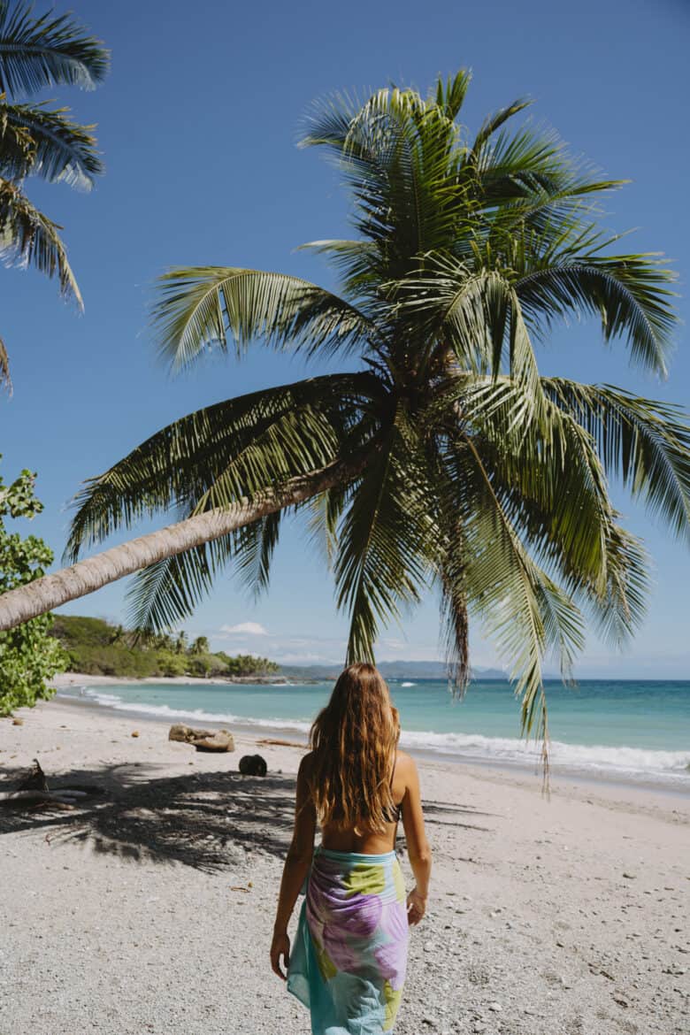 A woman walking on a beach near a palm tree in Montezuma, Costa Rica.