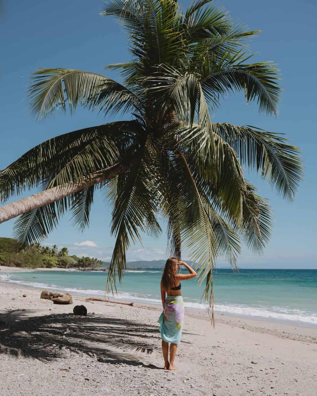 A woman standing under a palm tree on a beach in Montezuma, Costa Rica.