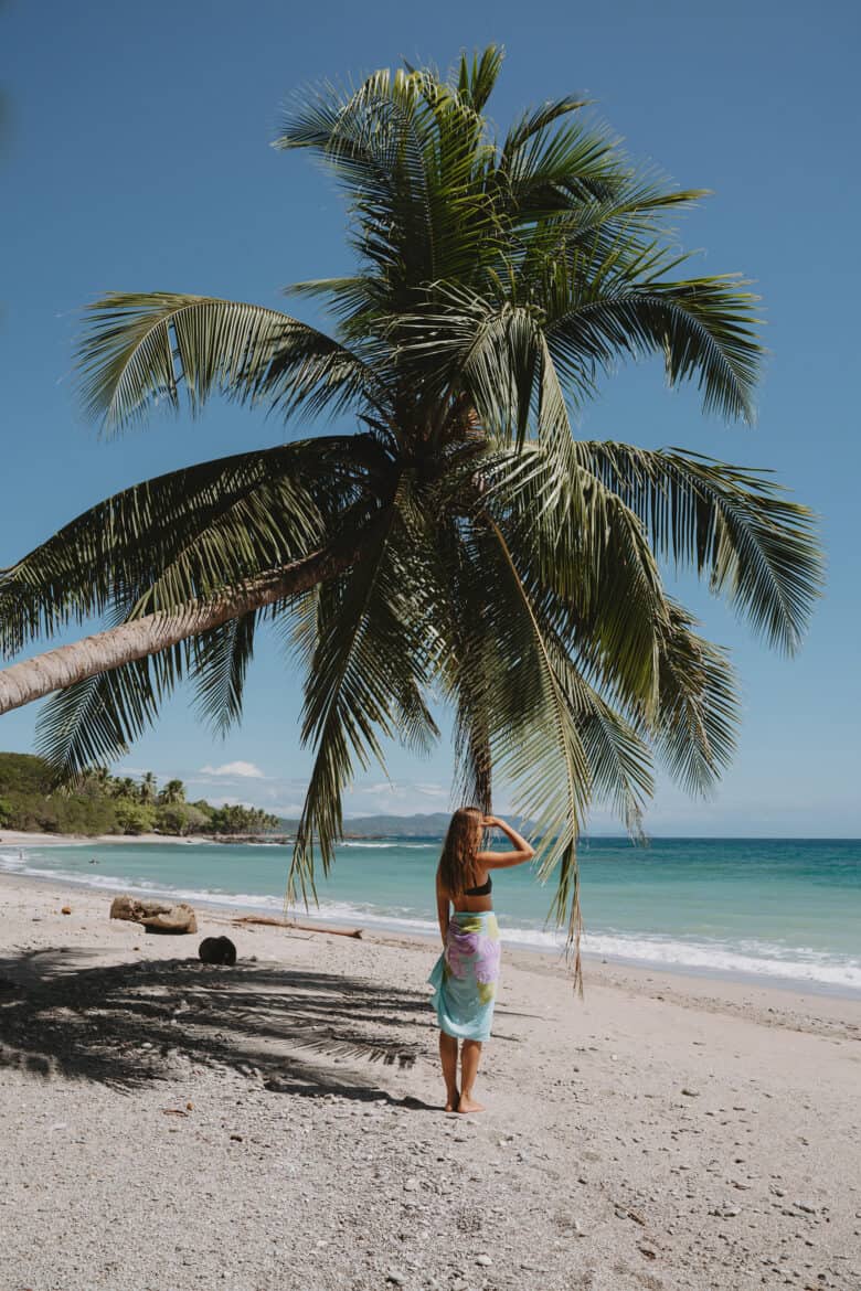 A woman standing under a palm tree on a beach in Montezuma, Costa Rica.